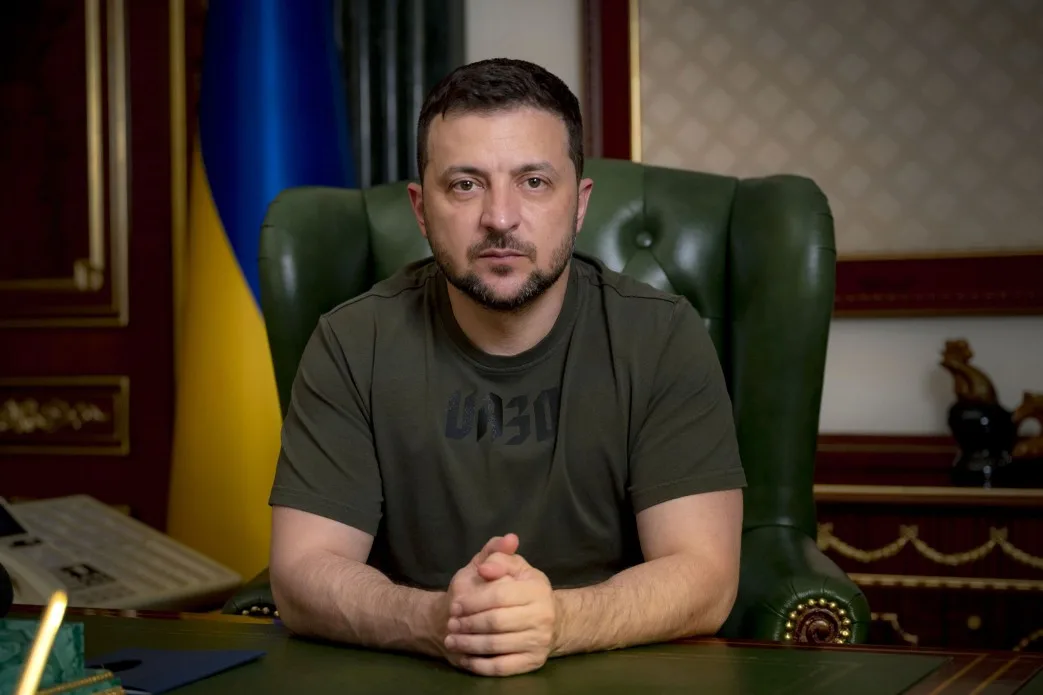 Президент Украины Владимир Зеленский выступает с обращением к нации после ракетного удара по торговому центру в Кременчуге, 27 июня 2022 года. Лидер стоит в тёмно-зелёной военной футболке, на фоне украинского флага.