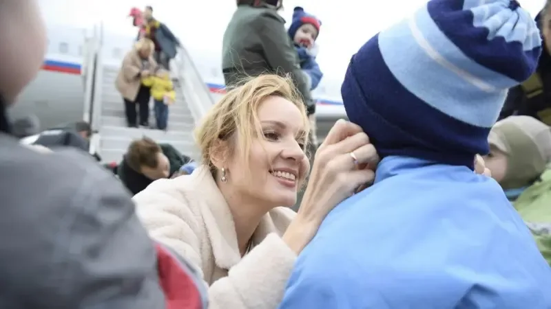 María Lvova-Belova recibe a niños ucranianos deportados junto a la escalerilla de un avión con los colores de la bandera rusa — la imagen de una «acogida humanitaria».