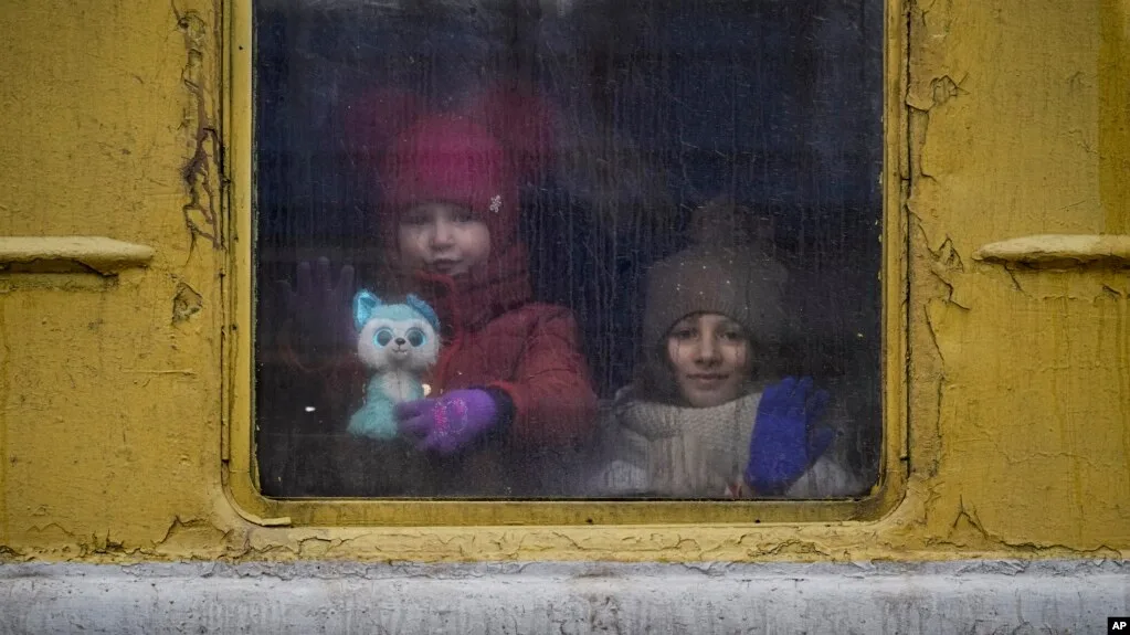Dos niños ucranianos miran por la ventanilla de un vagón de tren, uno abrazando un peluche — traslado de niños al interior de Rusia.